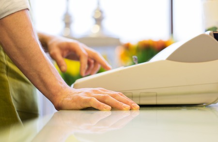 people, sale, retail, business and floristry concept - close up of florist man with cashbox standing at flower shop counter and countingの写真素材