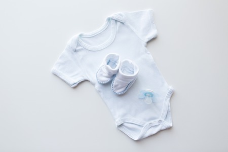 baby clothes, babyhood, motherhood and object concept - close up of white bodysuit, bootees and soother for newborn boy on tableの写真素材