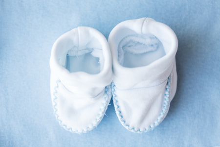 clothing, babyhood, motherhood and object concept - close up of white baby bootees for newborn boy on blueの写真素材