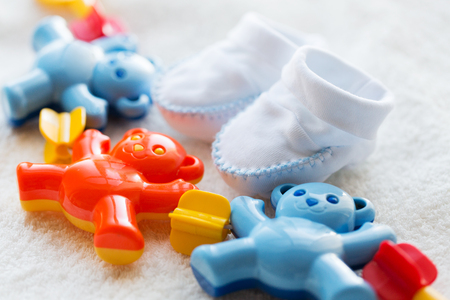 babyhood, childhood, toys, clothing and object concept - close up of baby rattle and bootees for newborn boy on towelの写真素材