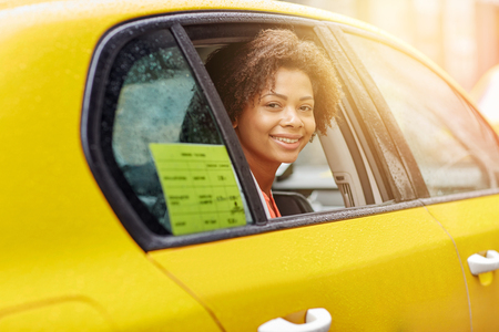 business trip, transportation and people concept - young smiling african american woman driving in taxi at city streetの写真素材