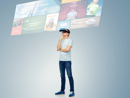 3d technology, virtual reality, entertainment, cyberspace and people concept - happy young man with virtual reality headset or 3d glasses thinking and looking at screen with internet newsの写真素材