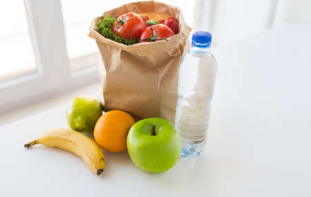 cooking, diet, vegetarian food and healthy eating concept - close up of paper bag with fresh ripe juicy fruits and vegetables and water bottle on kitchen table at homeの写真素材