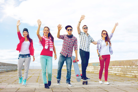 summer holidays and teenage concept - group of smiling teenagers waving hands outside
