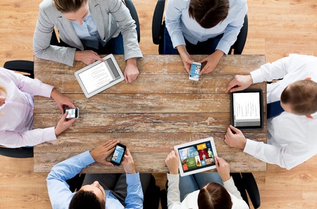 business, people, technology, media and team work concept - close up of creative team with smartphones and tablet pc computers sitting at table in officeの写真素材