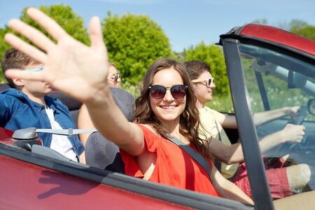 leisure, road trip, travel and people concept - happy friends driving in cabriolet car at country...