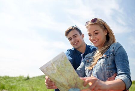 travel, tourism, summer vacation, location and people concept - happy couple with map outdoorsの写真素材