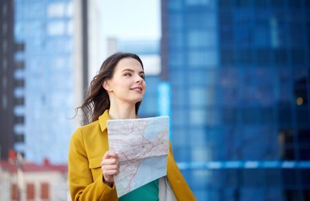 travel, trip, tourism, people and vacation concept - happy young woman with map walking along city...