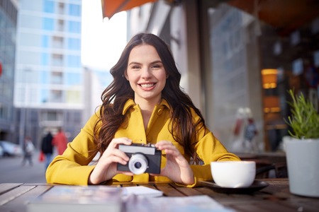 travel, tourism, photography, leisure and people concept - happy young tourist woman or teenage girl with film camera and guidebook drinking cocoa at city street cafe terraceの写真素材