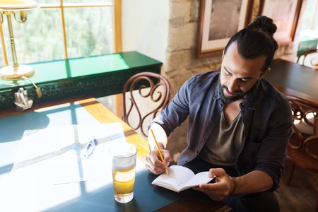 people, inspiration, freelance and leisure concept - man with beer writing to notebook at bar or pub