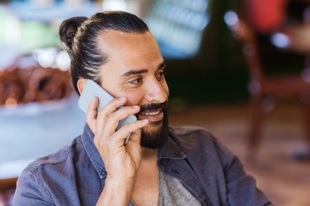 people, communication and technology concept - happy man calling on smartphone at bar or pub