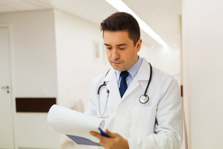medicine, healthcare and people concept - doctor writing to clipboard at hospitalの写真素材
