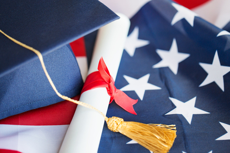 education, graduation, patriotism and nationalism concept - close up of bachelor hat and diploma on american flagの写真素材