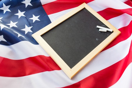 education, election, patriotism and nationalism concept - close up of blank school blackboard and chalk on american flagの写真素材
