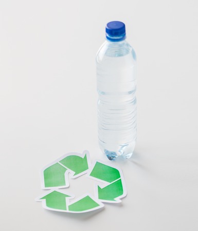 recycling, reuse, garbage disposal, environment and ecology concept - close up of plastic water bottle with green recycle symbol on tableの写真素材