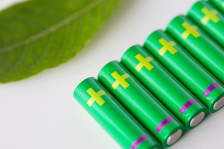 recycling, energy, power, environment and ecology concept - close up of green alkaline batteries and leafの写真素材