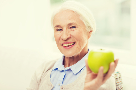 age, healthy eating, food, diet and people concept - happy smiling senior woman with green apple at homeの写真素材