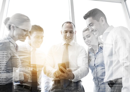 business, teamwork, people and technology concept - business team looking to smartphone in officeの写真素材