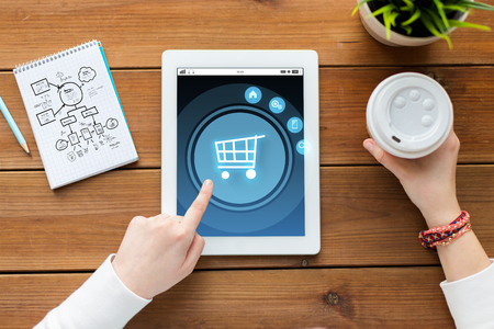 business, internet, technology and people concept - close up of woman with shopping cart on tablet pc computer screen, notebook and coffee on wooden tableの写真素材