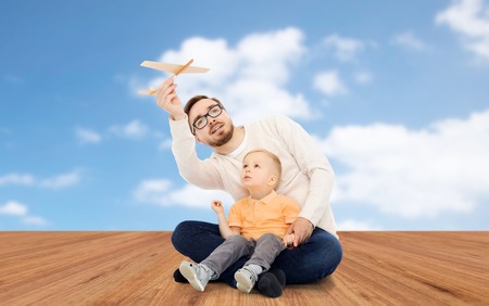 family, childhood, fatherhood, leisure and people concept - happy father and little son playing with toy airplane over blue sky and wooden floor backgroundの写真素材