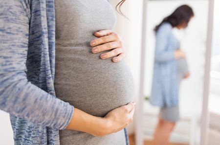 pregnancy, motherhood, people and expectation concept - close up of happy pregnant woman with big belly looking to mirror at homeの写真素材