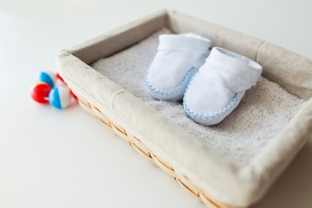 clothing, babyhood, motherhood and object concept - close up of white baby bootees for newborn boy on towel in basketの写真素材