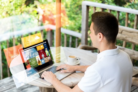 business, internet, media, people and technology concept - close up of businessman at laptop computer with news web page on screen outdoors on summer terrace and drinking coffeeの写真素材