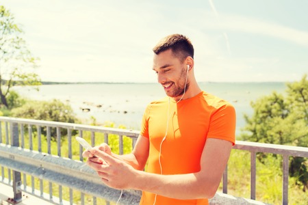 fitness, sport, people, technology and healthy lifestyle concept - smiling young man with smartphone...