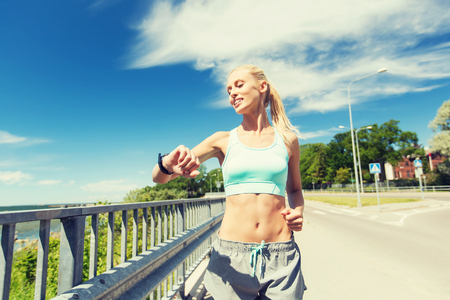fitness, sport, people, technology and healthy lifestyle concept - smiling young woman with heart rate watch running outdoorsの写真素材