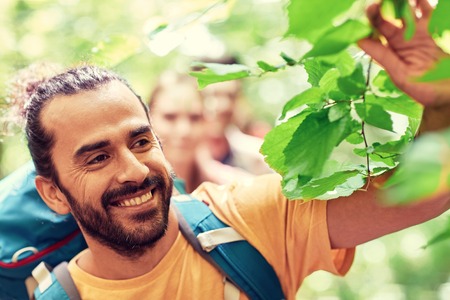 adventure, travel, tourism, hike and people concept - group of smiling friends walking with backpacks in woodsの写真素材