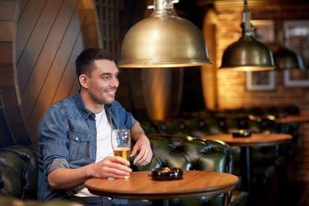 people, drinks, alcohol and leisure concept - happy young man drinking draft beer at bar or pubの写真素材