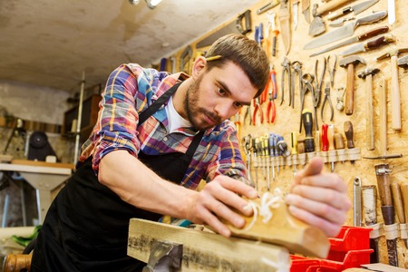 profession, carpentry, woodwork and people concept - carpenter working with plane and wood plank at workshopの写真素材