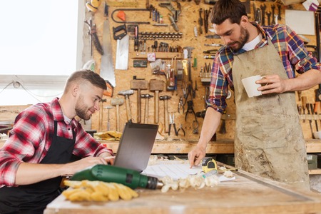profession, carpentry, technology and people concept - two carpenters with laptop computer and...