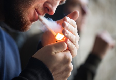 smoking, substance abuse, addiction and bad habits concept - close up of young people lighting...