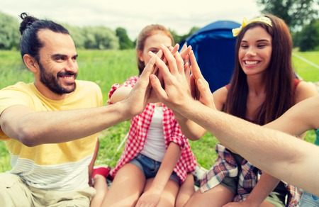 travel, tourism, hike and people concept - group of happy friends with tent making high five at campingの写真素材