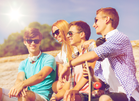 friendship, leisure, summer and people concept - group of smiling friends with skateboard sitting on city streetの写真素材