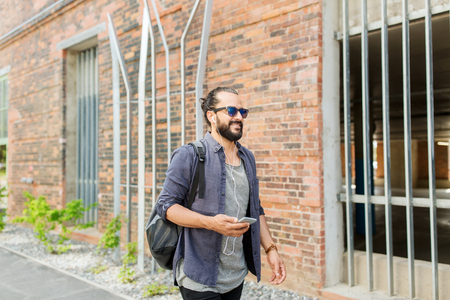 people, technology, travel and tourism - man with earphones, smartphone and bag walking along city street and listening to music の写真素材