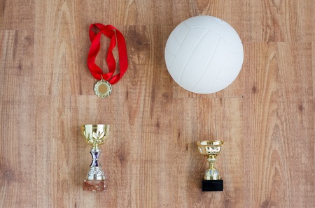 sport, achievement, championship, competition and success concept - close up of volleyball ball with golden medal and cup over wooden backgroundの写真素材