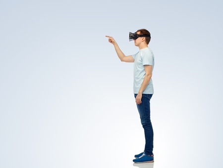 3d technology, virtual reality, entertainment, cyberspace and people concept - happy young man with virtual reality headset or 3d glasses playing game and touching somethingの写真素材