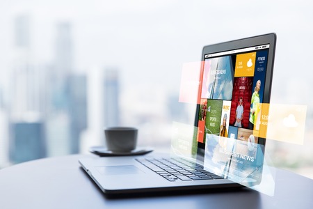 technology, internet, media, business and modern life concept- close up of open laptop computer with news web page on screen and coffee cup on table at office or hotel roomの写真素材