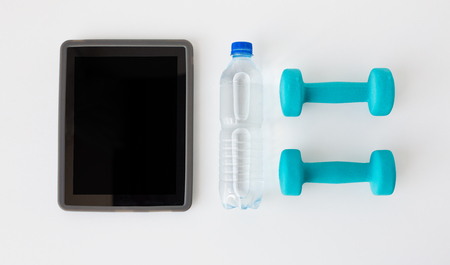 sport, healthy lifestyle and objects concept - close up of tablet pc computer with dumbbells and water bottle over white backgroundの写真素材