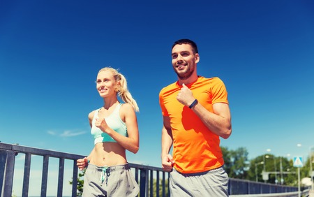fitness, sport, friendship and healthy lifestyle concept - smiling couple with heart-rate watch running at summer seasideの写真素材
