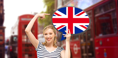 foreign language, english, travel, people and communication concept - smiling woman holding text bubble of british flag and pointing finger over london city street backgroundの写真素材