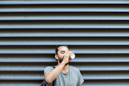 people, drinks, leisure and lifestyle - man drinking coffee from disposable paper cup on city streetの写真素材