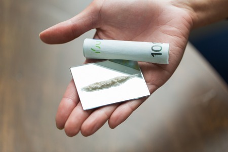 drug use, people, addiction and substance abuse concept - close up of addict hand with crack cocaine drug dose track on mirror and money rollの写真素材