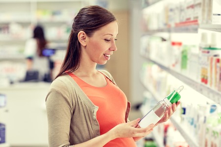 pregnancy, medicine, pharmaceutics, health care and people concept - happy pregnant woman choosing anti stretch marks lotion at pharmacyの写真素材
