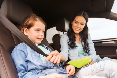 family, transport, road trip and people concept - happy woman fastening child with safety seat belt...