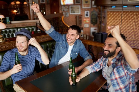 people, leisure, friendship and bachelor party concept - happy male friends drinking bottled beer and having fun at bar or pubの写真素材
