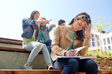 education, bullying, high school, social relations and people concept - unhappy student girl with book suffering of classmates mockeryの写真素材