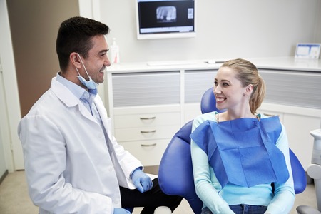 people, medicine, stomatology and health care concept - happy male dentist with woman patient talking at dental clinic officeの写真素材